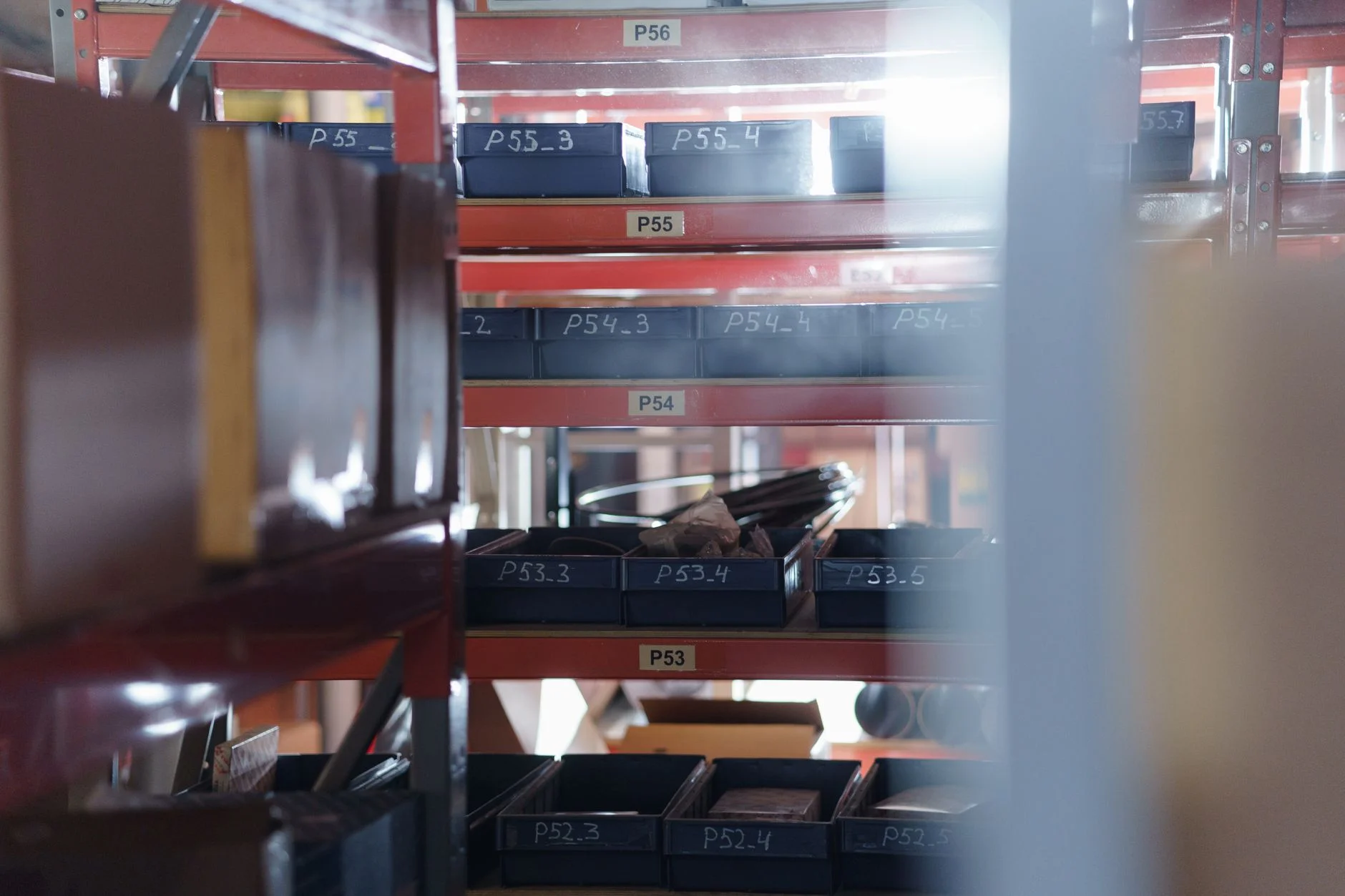 Warehouse racking of parts bins labelled P53 through P56, each code meaningful only inside the company that assigned it